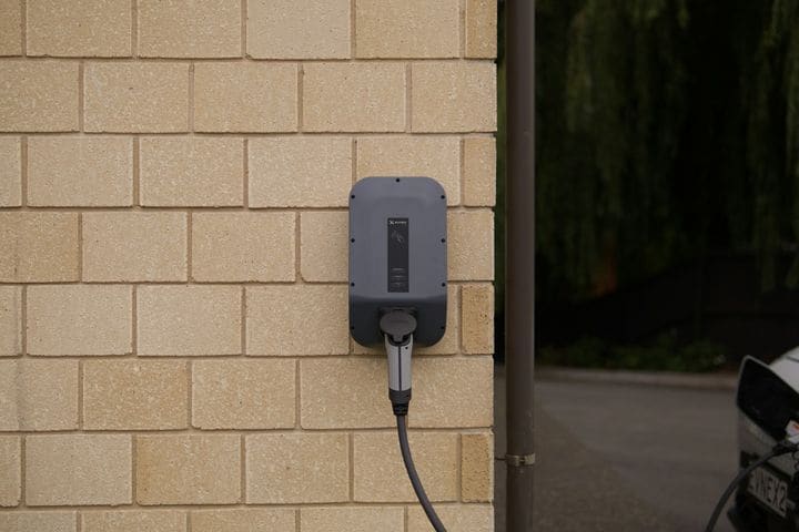 Grey Evnex wall charger with its cable plugged in, mounted on a light sandstone block wall