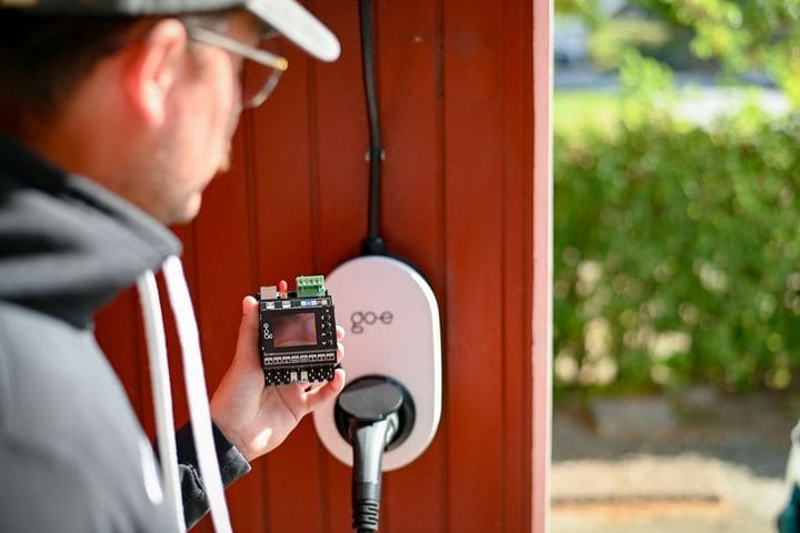 Installer holding a control module next to a white go-e wall charger on a red timber wall