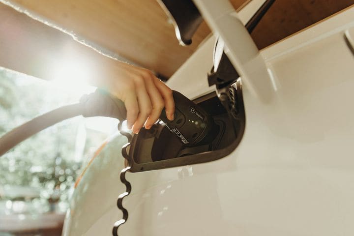 Hand plugging a Type 2 charging connector into the charge port of a white electric car