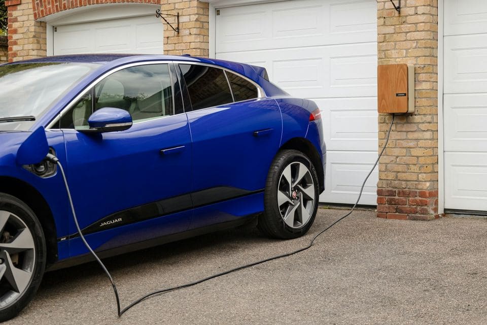Blue Jaguar I-Pace charging from a timber-fronted wall charger between two garage doors