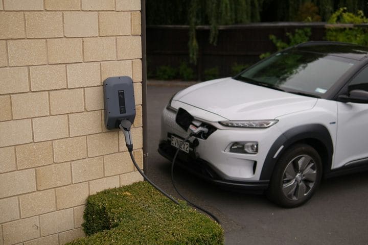 Grey Evnex wall charger on a sandstone-coloured wall, charging a white Hyundai Kona parked in the driveway