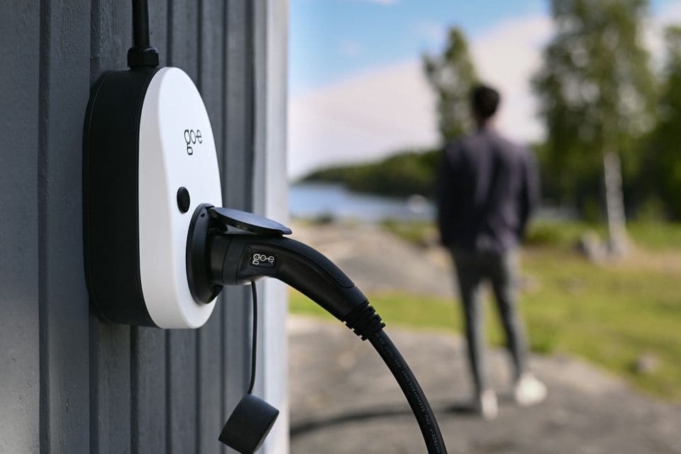 Close-up of a white go-e wall charger with its Type 2 cable plugged in, on a dark timber wall