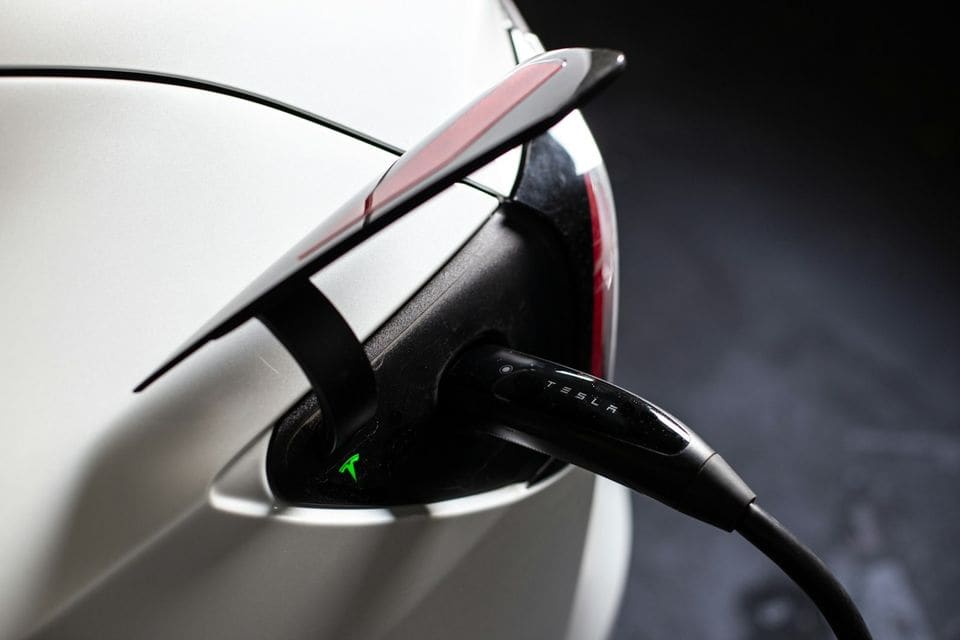Tesla charging connector plugged into the charge port of a white Tesla, the port light glowing green