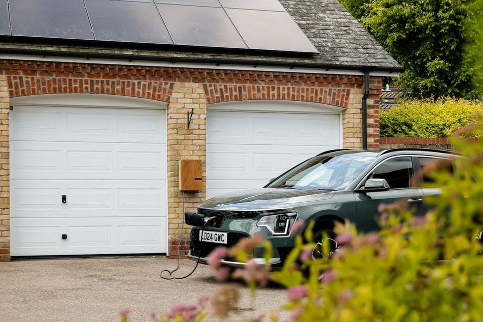 Green electric SUV charging in front of a double garage with solar panels on the roof