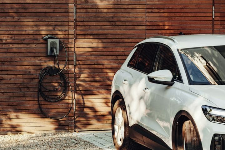 Wall-mounted EV charger with its cable coiled on a timber-clad wall, a white SUV parked alongside
